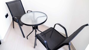 A small, round glass table with a metal frame, accompanied by two black mesh chairs. - Stayshort - Amazing Studio in JVC That Sleeps 2 With Balcony (Dubai)