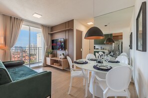 Een moderne woonkamer met een groene bank, een eettafel gedekt voor vier personen, en een keuken op de achtergrond.