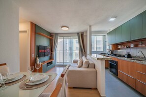 A modern kitchen with a dining area, a sofa, and a TV displaying 'NETFLIX'. - Mirante #1302 - Apto in Fortaleza by Carpediem (Fortaleza)