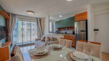 Una sala de estar moderna con comedor, ventanas amplias y una cocina al fondo.