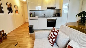 Ett kompakt bostadsutrymme med ett litet kök, en soffa med mönstrade kuddar och ett trägolv.