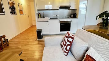 A compact living space with a kitchenette, a sofa with patterned cushions, and a wooden floor.