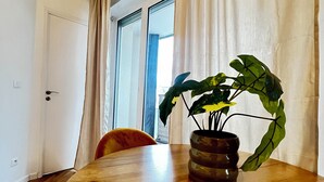 Ett matbord i trä med en krukväxt, en stol och ett fönster med gardiner.