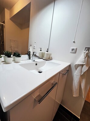 A modern bathroom with a white sink, two potted plants, a mirror, and a towel rack. - Modern Apartment Near Paris & Orly • Pvt Parking (Athis-Mons)