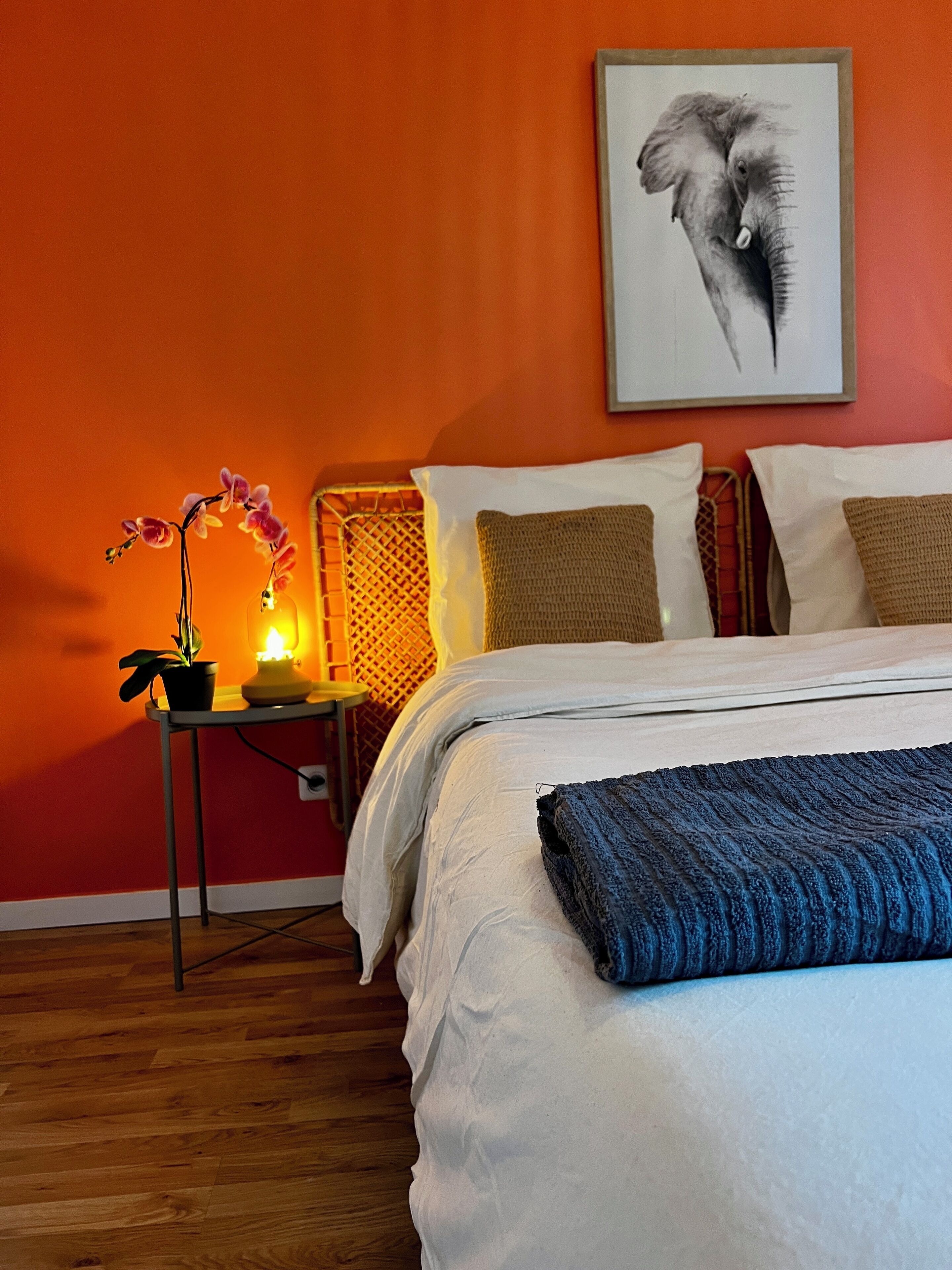 A bedroom with a bed, pillows, a nightstand with a lamp, and a framed picture on the wall.