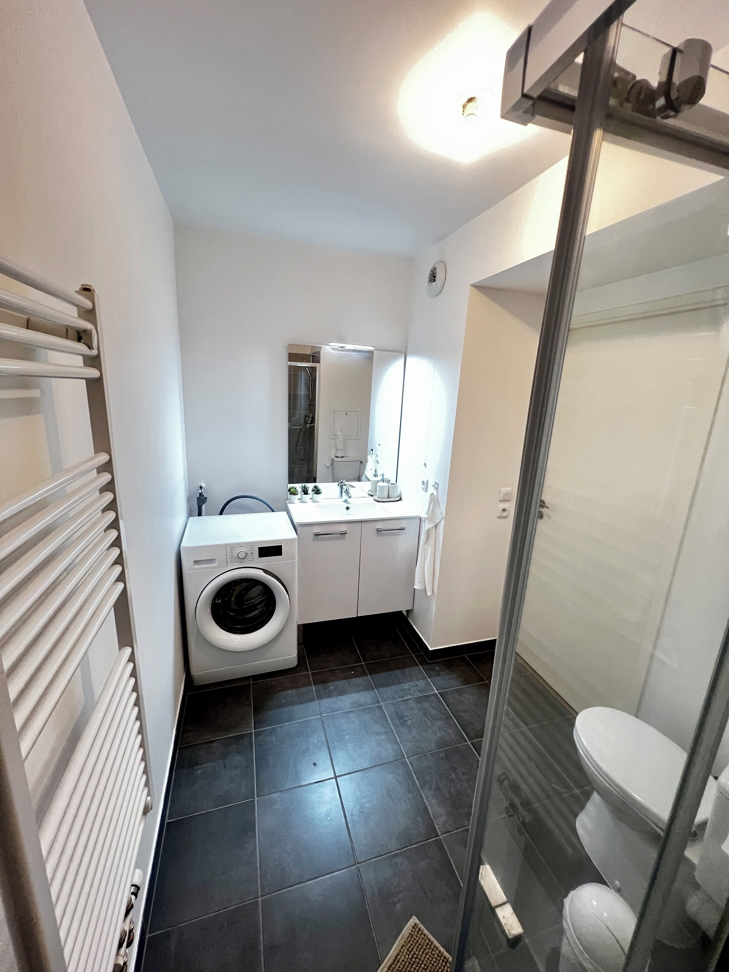 A compact bathroom with a washing machine, a sink, a mirror, and a toilet.