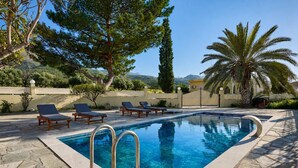 A swimming pool with lounge chairs, surrounded by trees and a stone wall. - Creta Leisure Escape, Private Pool & Garden Oasis (Pompia)
