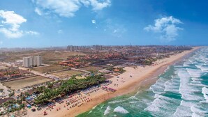 An aerial view of a coastal city with a wide beach, high-rise buildings, and a clear sky. - Mirante #1004 - Comfortable Apartment by Carpediem (Fortaleza)