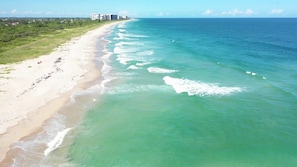 Une plage avec une eau turquoise et limpide, un rivage sablonneux et des bâtiments en arrière-plan.