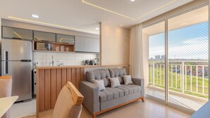 Eine moderne Wohnung mit Küche, einem grauen Sofa und einem Balkon mit Blick auf die Stadt.