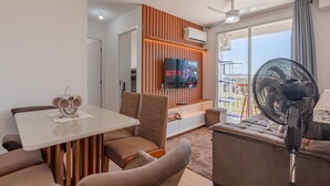 A modern living room with a flat-screen TV, a ceiling fan, and a dining area with a table and chairs. - Mirante #804 - Apartment in Fortaleza by Carpediem (Fortaleza)