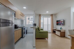 A modern kitchen with a built-in oven and a dining area with a green sofa and a TV mounted on the wall. - Mirante #607 - Apartment in Fortaleza by Carpediem (Fortaleza)