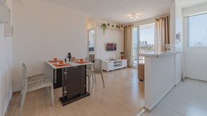 A modern living room with a dining area, a TV mounted on the wall, and a large window with curtains. - Mirante Clube #606 - Apto 2 Quartos by Carpediem (Fortaleza)