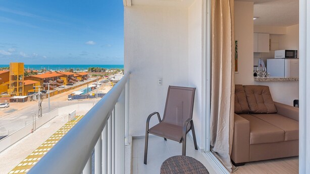 A balcony with a view of the beach, a brown chair, and a brown sofa. - Mirante Clube #606 - Apto 2 Quartos by Carpediem (Fortaleza)