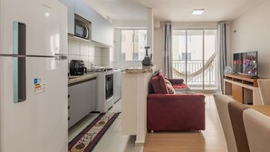 A compact living space with a kitchenette, a red sofa, a TV, and a balcony with a hammock. - Mirante #407 - Two-bedroom Apt By Carpediem (Fortaleza)