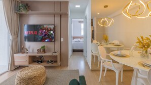 A modern living room with a flat-screen TV, a dining area with white chairs and a table set for two, and a hallway leading to a bedroom. - Mirante #307 - Space and Style by Carpediem (Fortaleza)