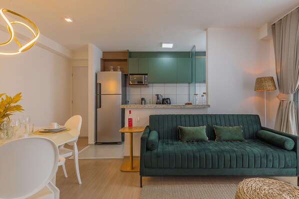 A modern living room with a green sofa, a dining table with chairs, and a kitchen area in the background. - Mirante #307 - Space and Style by Carpediem (Fortaleza)