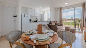 A modern living room with a dining area, a kitchen, and a balcony with a city view. - Mirante #303 2 Suites Praia Futuro by Carpediem (Fortaleza)