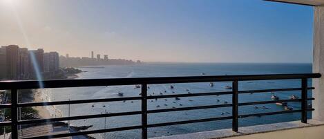 A balcony with a view of a beach and the ocean, featuring a railing and a clear sky.