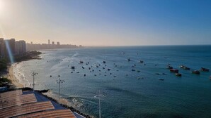 A coastal cityscape with a marina filled with boats, a beach, and high-rise buildings in the background. - Iate Plaza #1404 - Studio Vista Mar por Carpediem (Fortaleza)