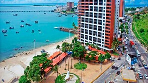 A coastal hotel with a view of the sea, a parking area, and a road with vehicles. - Iate Plaza #1404 - Studio Vista Mar por Carpediem (Fortaleza)