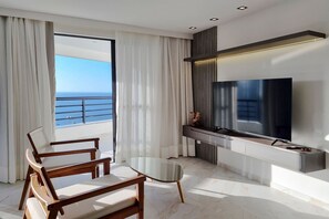 A modern living room with a large TV, wooden furniture, and a view of the ocean. - Iate Plaza #1404 - Studio Vista Mar por Carpediem (Fortaleza)