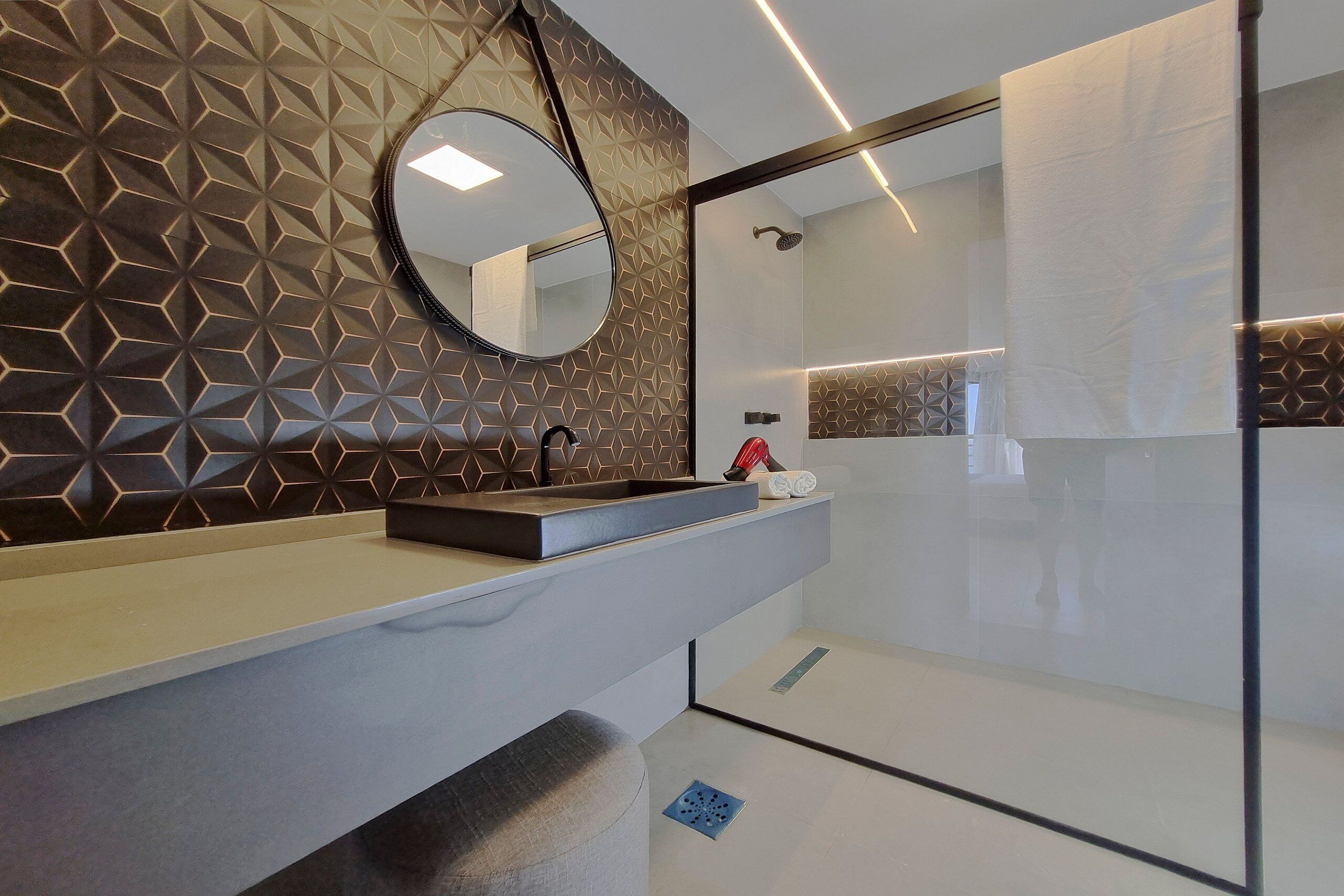 A modern bathroom with a geometric patterned wall, a round mirror, a sink with a towel holder, and a shower area.
