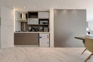 A modern kitchen with built-in appliances, a refrigerator, and a dining area with a chair. - Iate Plaza #1404 - Studio Vista Mar por Carpediem (Fortaleza)