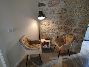 A room with two armchairs, a stone wall, a small table with a vase, and a lamp.