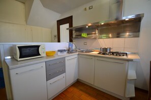 Een kleine keuken met witte kastjes, een magnetron, een gasfornuis en een spoelbak.