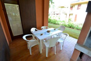Een terras met tafel en stoelen, een betegelde vloer en uitzicht op een gebouw en groen.