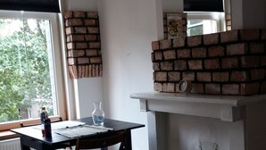 Ett rum med en tegelbeklädd öppen spis, ett matbord med stolar och ett fönster med persienner.