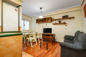 Una sala de estar con un sofá, televisión, estanterías de madera y una zona de comedor con sillas y una mesa.