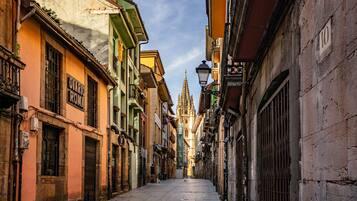 A narrow street with historic buildings, a cathedral spire, and a street lamp.
