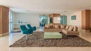 A modern living room with a beige sectional sofa, a glass coffee table, and a blue chair. - Hiperion #502 - Apt in Fortaleza by Carpediem (Fortaleza)