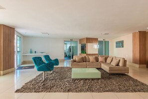 A modern living room with a beige sectional sofa, a glass coffee table, and a blue chair. - Hiperion #502 - Apt in Fortaleza by Carpediem (Fortaleza)