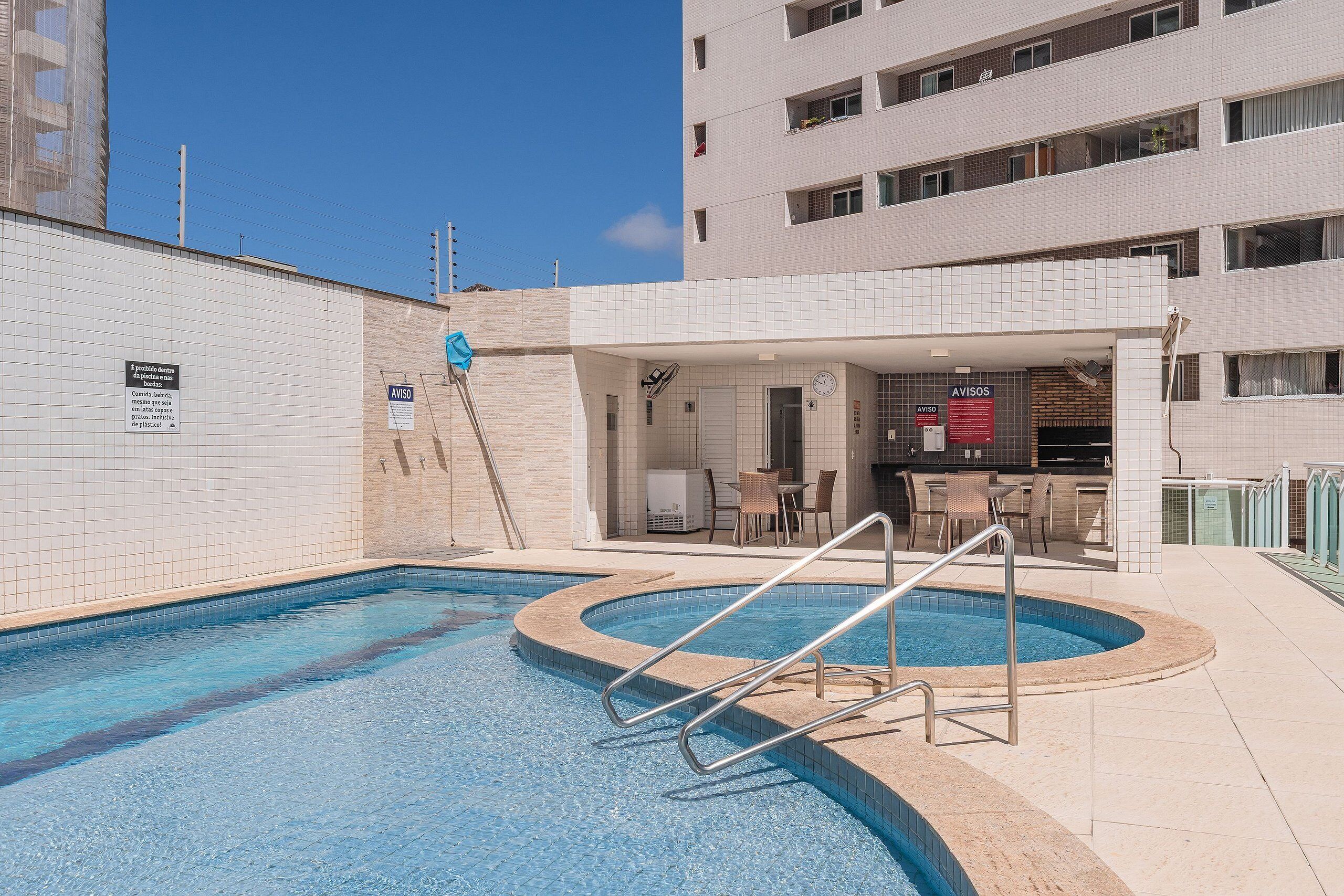 A swimming pool with a metal ladder, a restaurant area, and a building with multiple floors.