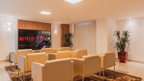 A modern lounge area with leather chairs, a large flat-screen TV displaying 'NETFLIX', and a potted plant. - Hiperion #502 - Apt in Fortaleza by Carpediem (Fortaleza)