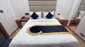 Hotellihuone, jossa on sänky, yöpöydät, peili ja seinäpistorasia.