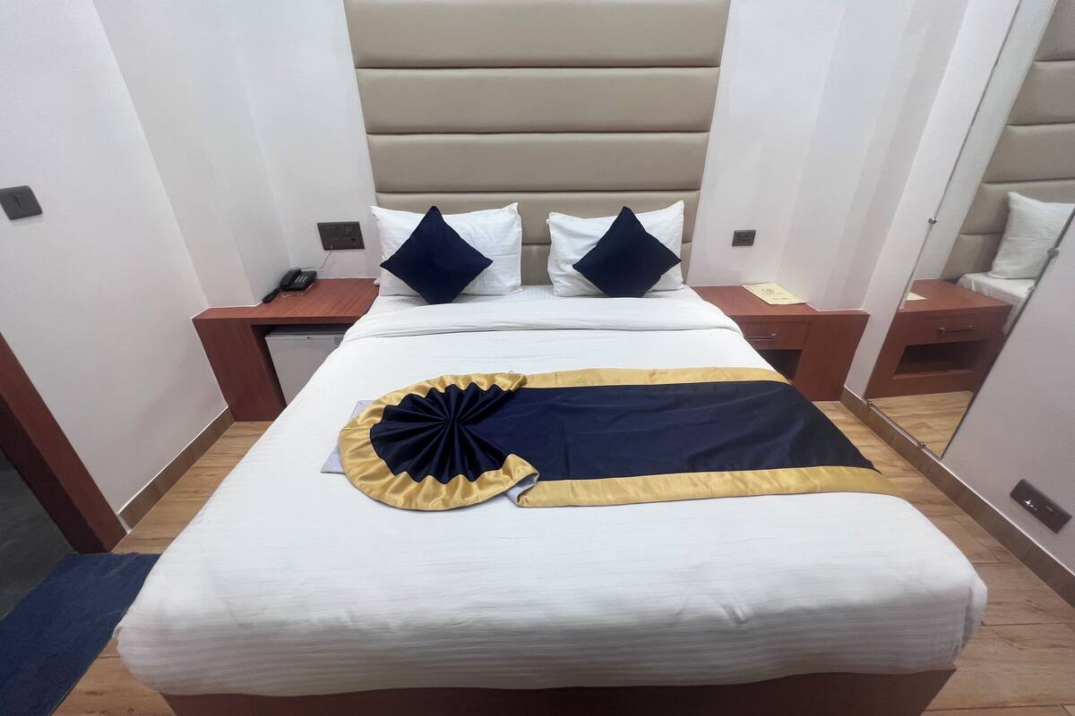Una habitación de hotel con cama, mesitas de noche, un espejo y un enchufe.