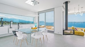 Zona pranzo moderna con tavolo in vetro, sedie bianche e vista sul mare.