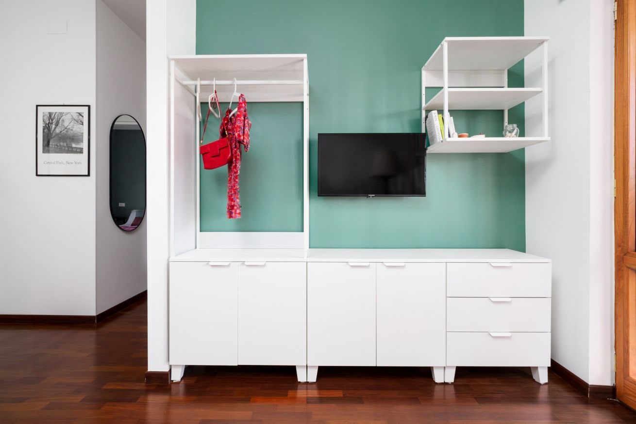 A white dresser with drawers and shelves, a flat-screen TV, and a red garment hanging on a rack.