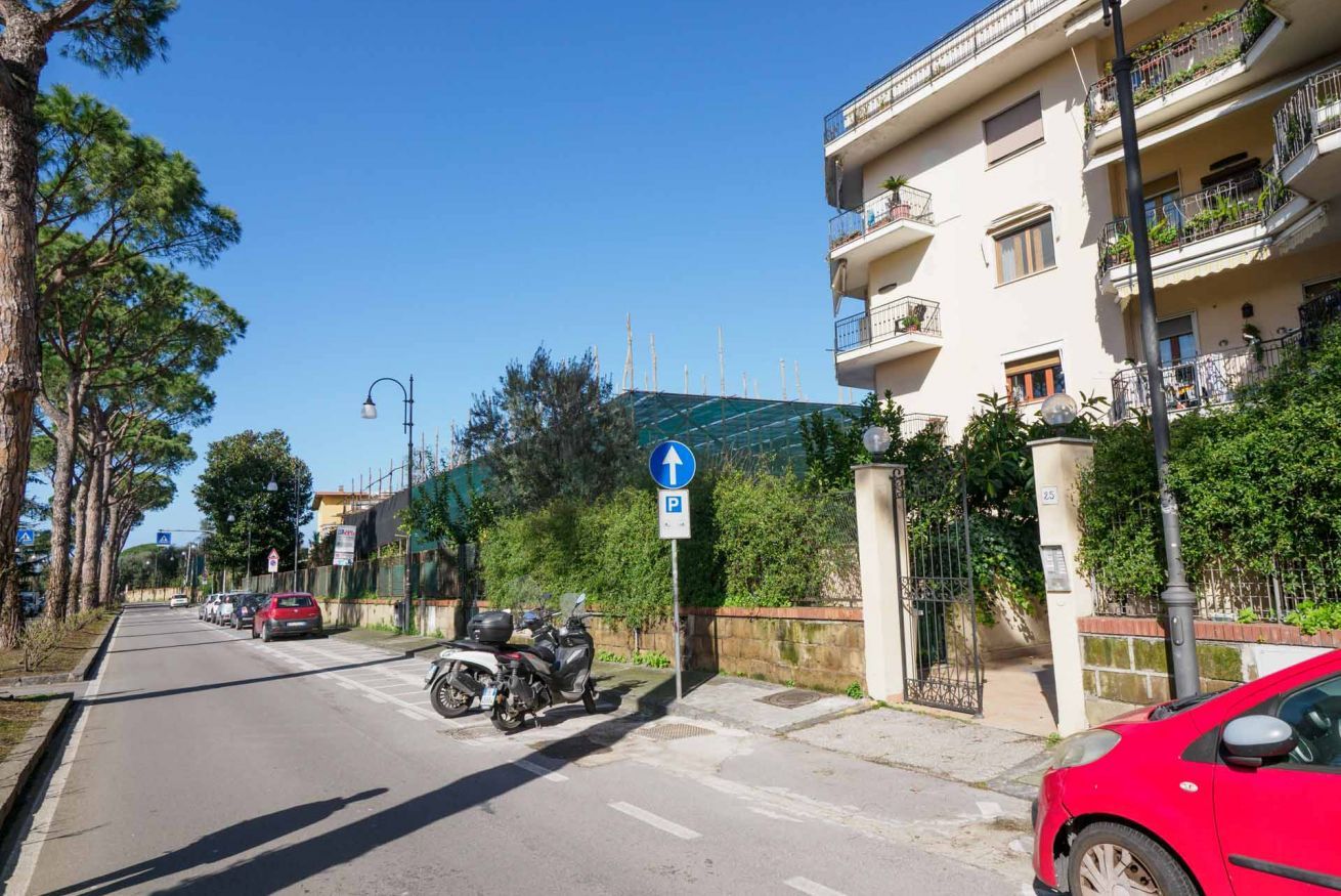 A street with parked cars and a motorcycle, a blue parking sign, and a building with balconies.