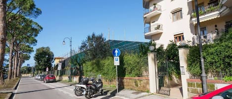 A street with parked cars and a motorcycle, a blue parking sign, and a building with balconies.