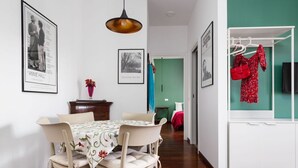 Un comedor con una mesa dispuesta para cuatro, una lámpara colgante y un armario blanco con un bolso rojo colgado.