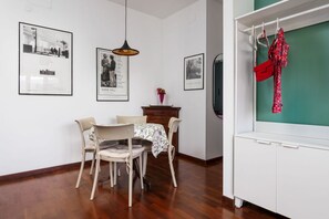 Un coin repas avec une table et des chaises, des tableaux encadrés au mur, un luminaire suspendu et un meuble blanc sur lequel est posé un objet rouge.