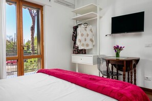Une chambre à coucher comprenant un lit, un bureau, une chaise, un téléviseur et une fenêtre donnant sur des arbres.