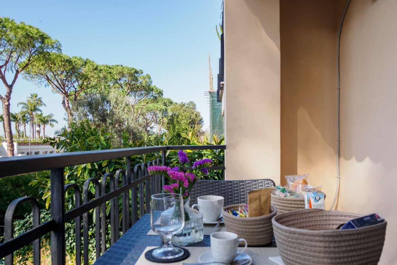 A balcony with a table set for two, a glass, a white mug, and woven baskets.