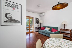 Ein Zimmer mit einem grünen Sofa, einem Bett mit floralem Überwurf, einem Holznachttisch, einer Hängelampe und einem Poster an der Wand.