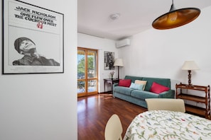 A room with a green sofa, a bed with a floral bedspread, a wooden side table, a hanging lamp, and a poster on the wall. - La Perla Rara | Stylish Apartment with Balcony Near Sorrento (SANT'AGNELLO)